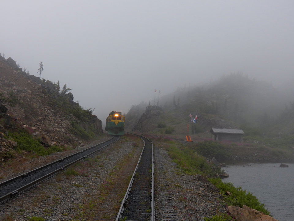 Flags emerge from the mist at the border crossing on the WP&Y RR - by Peter T. Rossi